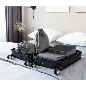 Ein schwarzer Koffer liegt offen auf einem aufgeräumten Bett, gefüllt mit grauen Packwürfeln, Beuteln und dem Bigso TRAVEL Wäschesack Grau - 2 Stk. - ideal für jede Reise. Gedämpftes Licht, weiße Kissen und minimale Dekoration vervollständigen die Szene.
