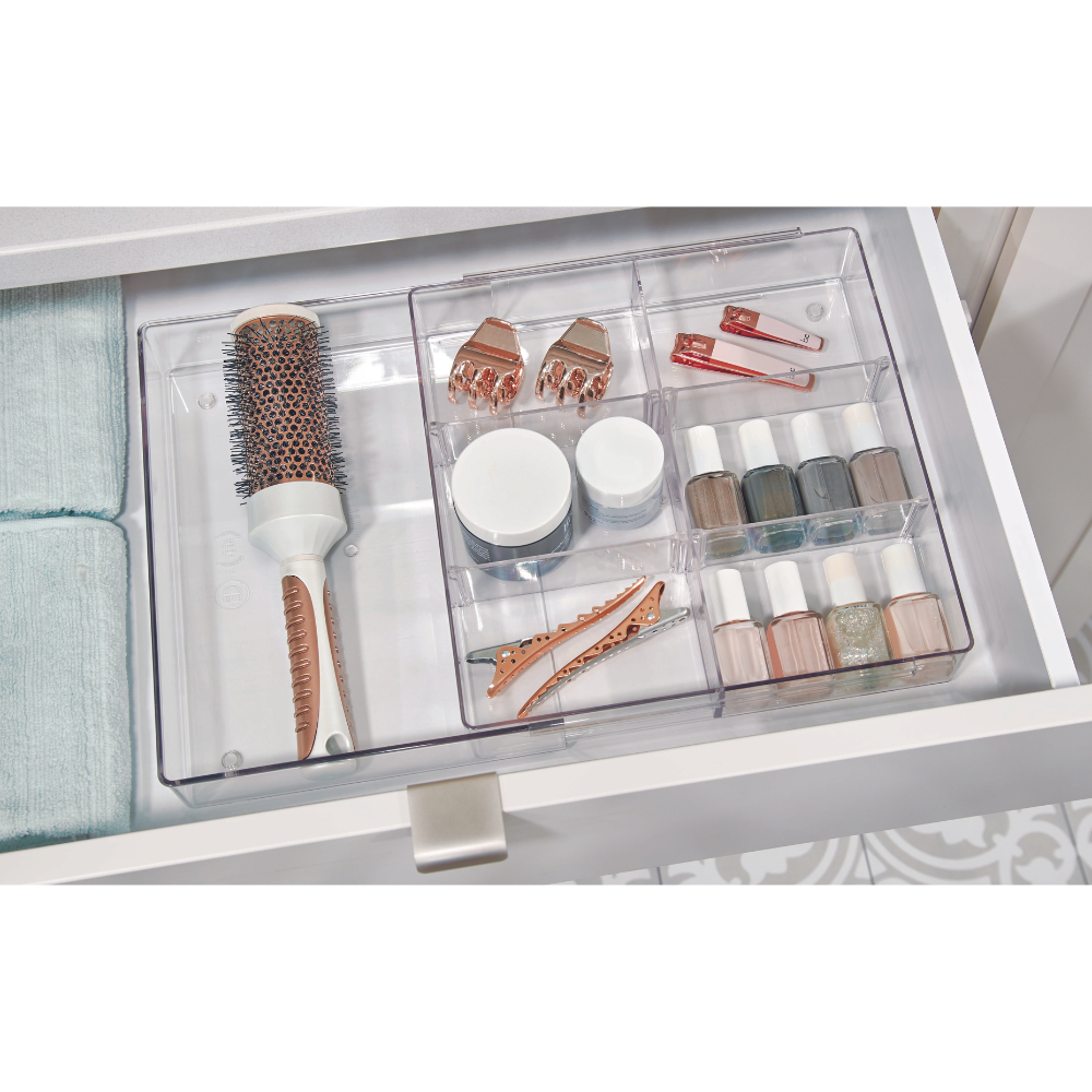 Der HOME EDIT - Schubladen Organizer KLAR ausziehbar von iDesign bewahrt in einer weißen Schublade eine runde Haarbürste, Haarspangen, Nagellack und kleine Döschen übersichtlich neben gefalteten Handtüchern auf.