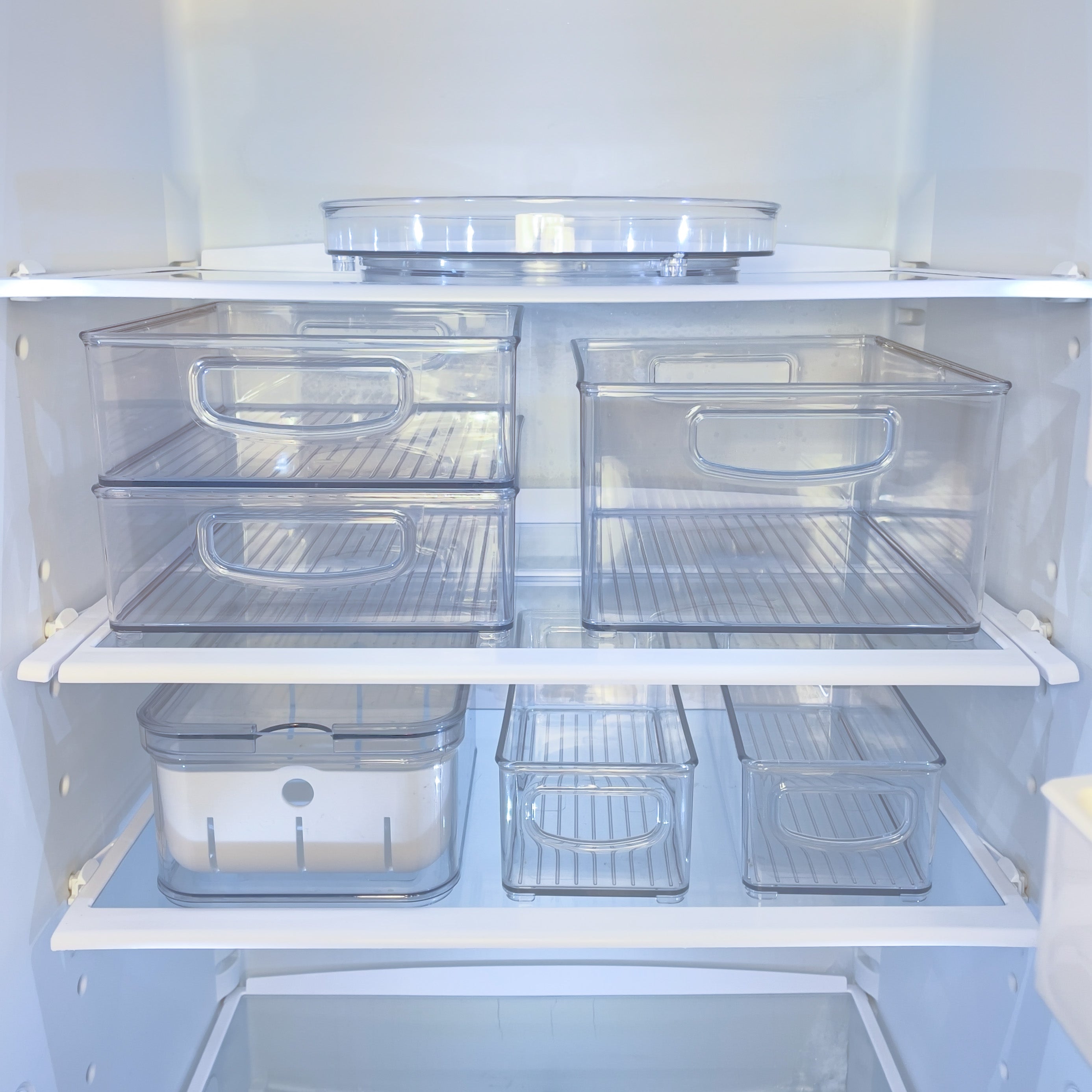 Transparente Plastikboxen in leerem Kühlschrank, geordnet auf Regalen.