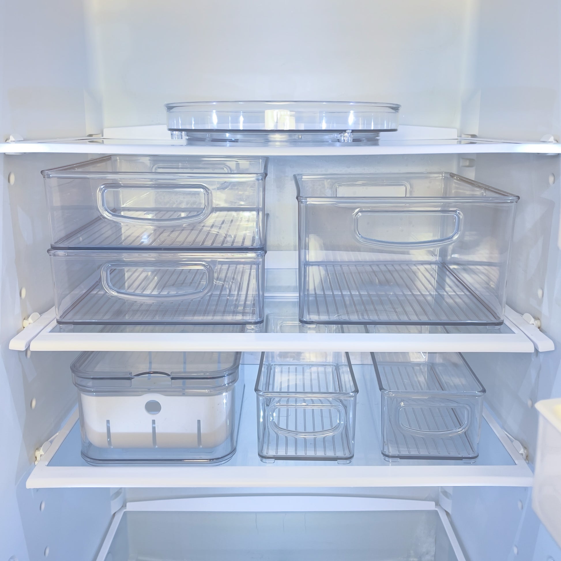 Transparente Plastikboxen in leerem Kühlschrank, geordnet auf Regalen.
