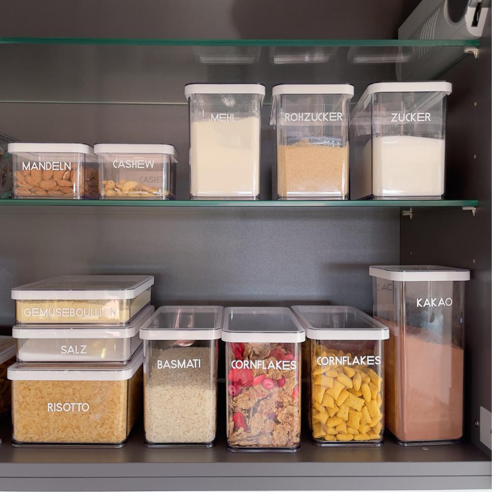 Shelf with storage containers for almonds, cashews, flour, sugar, raw sugar, salt, rice, cornflakes, cocoa.