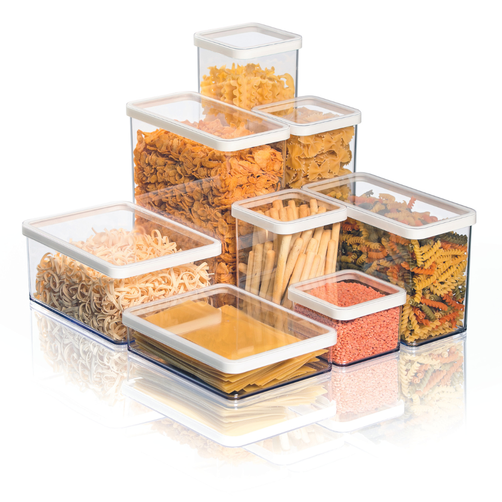 Transparent plastic containers with pasta and grains, lined up on a reflective white surface.