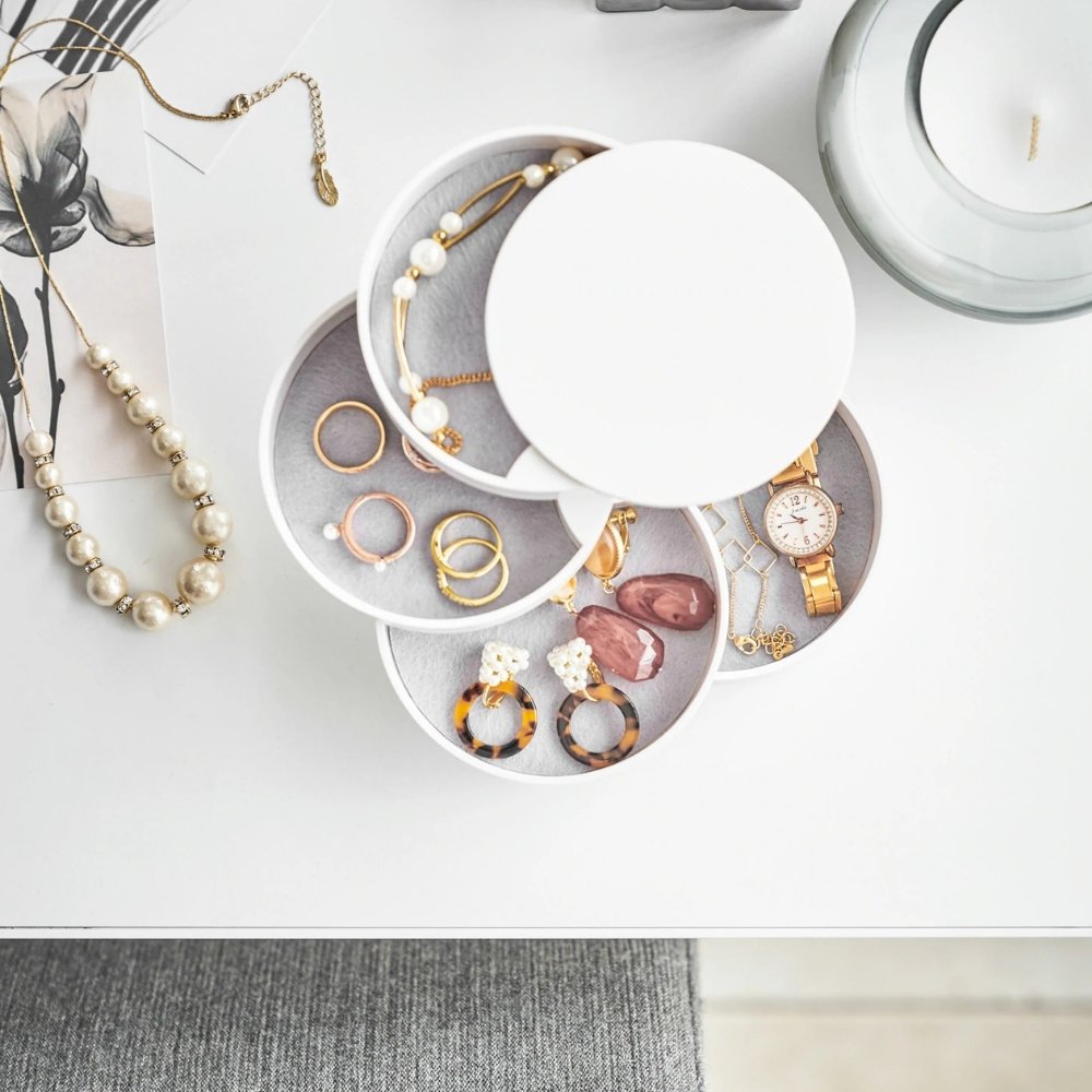 Schmuckschatulle, geöffnet, zeigt Ringe, Armband, Ohrringe und Uhr auf weißem Tisch.